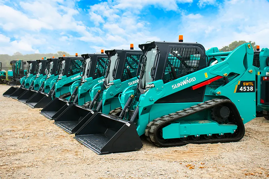 A row of blue construction equipment parked in the sand.